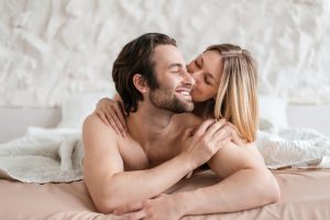 Affectionate young couple lying together in bed, hugging and kissing after lovemaking. Intimate relationship concept