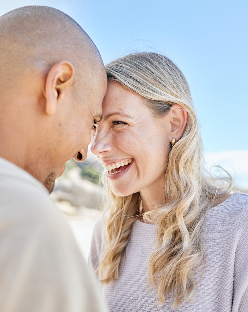 Intimate romantic couple bonding during a date. Mature loving interracial man and woman laughing and spending time together at the beach standing close to each other and smiling affectionately.